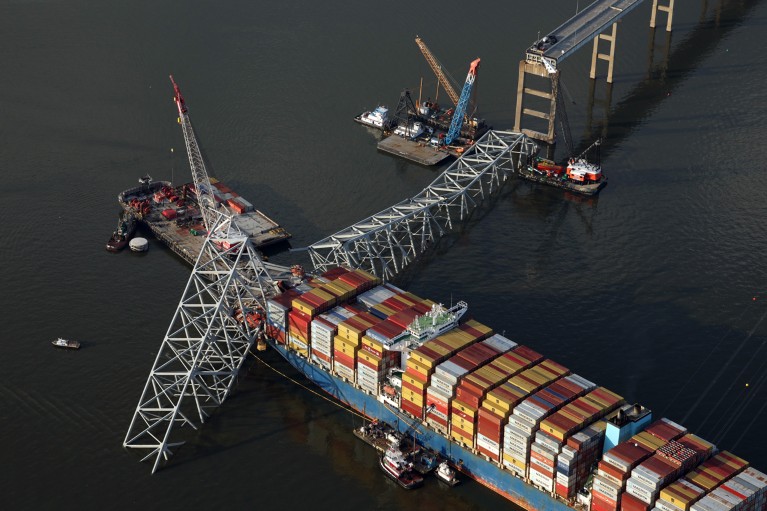 Aerial view of salvage crews using cranes to remove bridge wreckage from the cargo ship