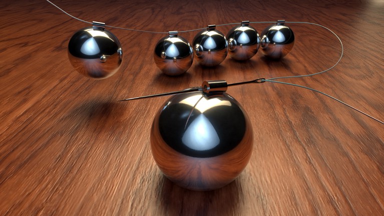 The metal balls from a Newton’s cradle sit on a table surface, all linked together by a needle and thread