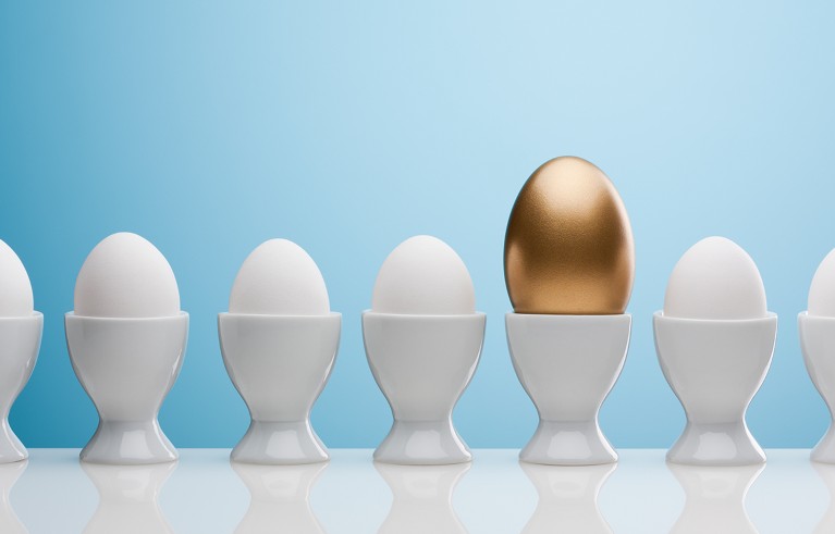 Golden egg in egg cup among other eggs in line.