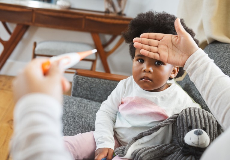 A mother checks her toddler daughter's temperature on the sofa