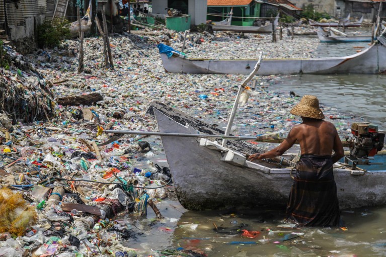 A fisher in Indonesia brings his boat to a shoreline covered in discarded plastic rubbish