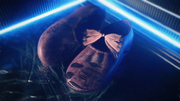 A worn pair of baby shoes with a frayed pink bow sit on a shiny floor, framed by neon lights