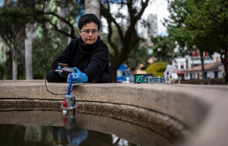 Alba Graciela Ávila Bernal crouches behind a fountain while measuring water parameters with a device in her hands.