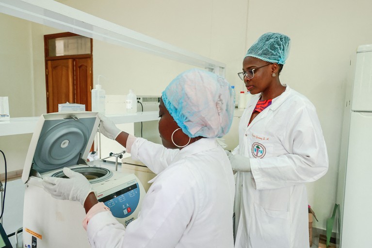 Two researchers in protecteive clothing using a centrifuge in a medical research laboratory.