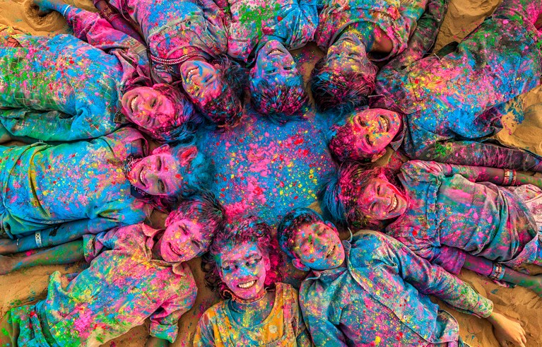 Top shot of a group of happy children lying in a circle with their heads together, all covered in coloured powder for Holi.