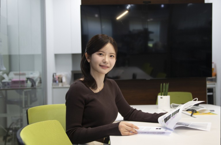 Yunhee Kim sitting at a lab desk with paperwork.