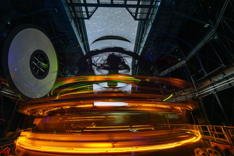 A long-exposure photograph taken from inside the Vera C. Rubin Observatory's telescope dome, with bright orange light trails under the starry sky visible through the roof