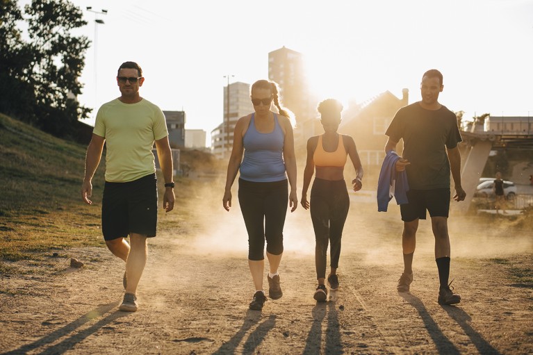 Four people in athletic wear walking on a dirt path on a sunny day.