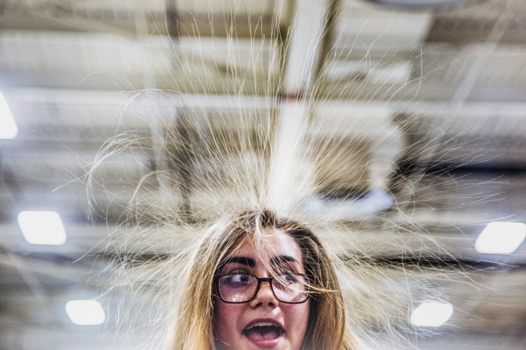 A close-up of a girl wearing glasses with her long hair standing on end and a shocked expression on her face.