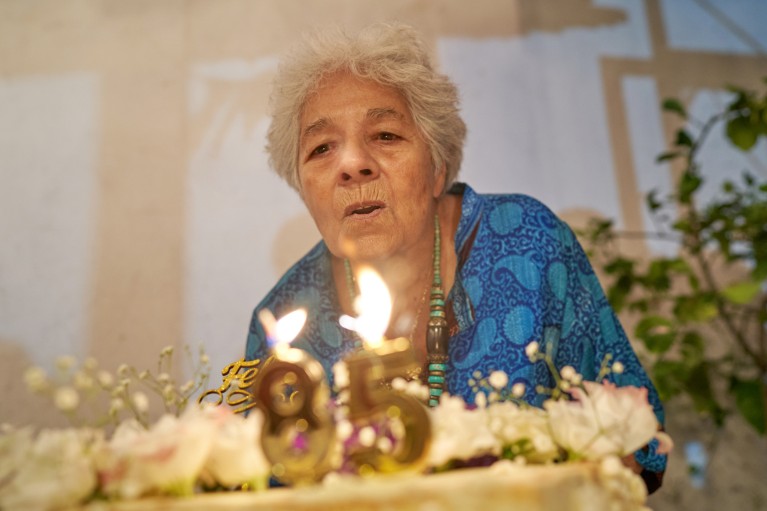 A close-up of an elderly woman blowing out candles on her 85th birthday cake