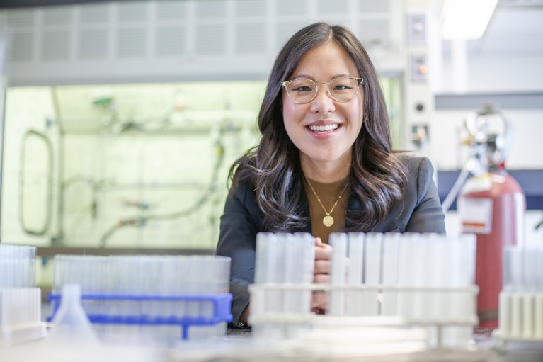 Christine Le smiles in her laboratory, rows of test tubes fill the foreground.