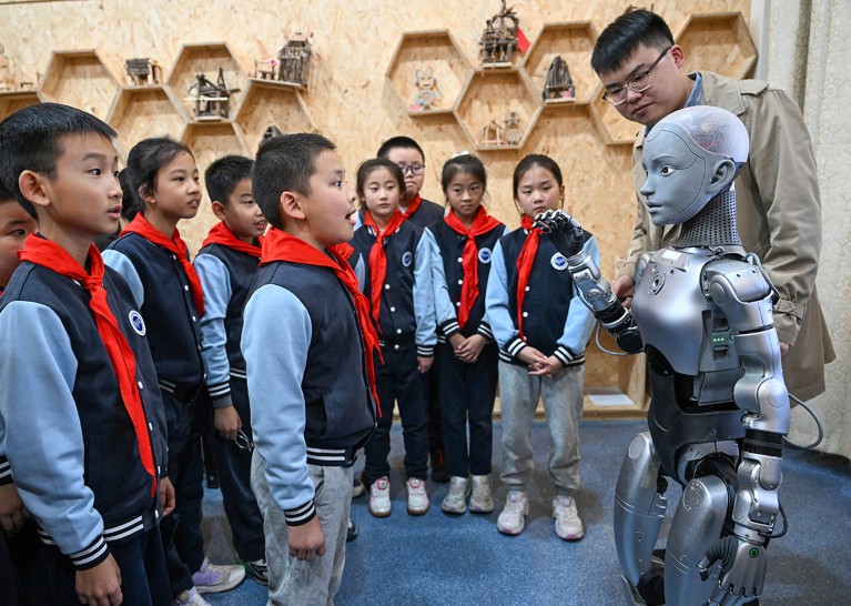 A group of students from a primary school stand and watch a humanoid robot named "Xiao An” in a classroom area in China.