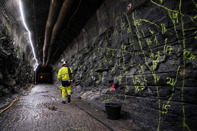 person in fluorescent clothing and helmet walking inside a tunnel.