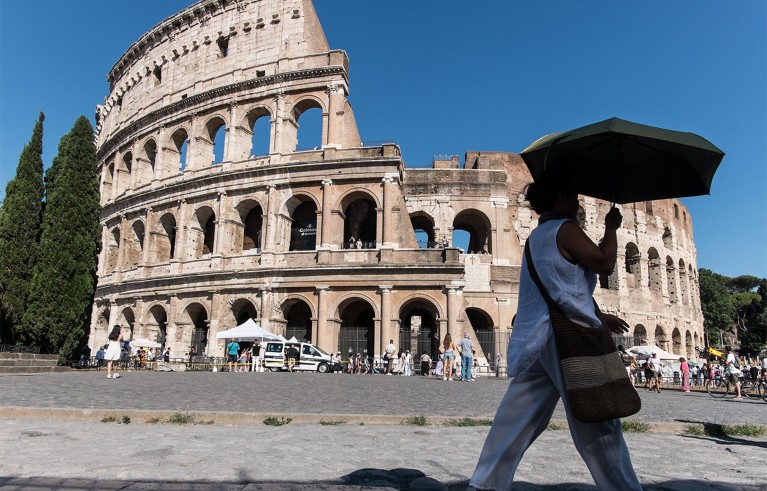 A person carrying an umbrella walks past the Colosseum in Rome.