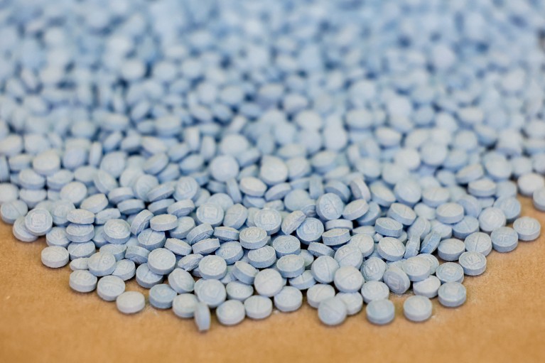 A large pile of small, round, light blue pills scattered across a surface.