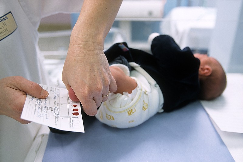 A baby getting a blood screening via heel prick by a nurse.