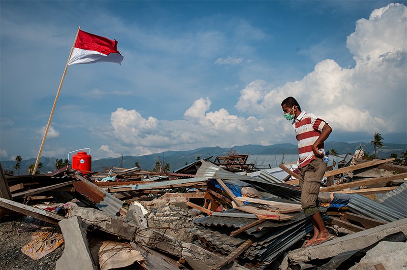 A man in a red striped tshirt walks over a ruined building in South Palu